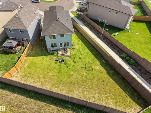 Expansive fenced backyard with a light blue exterior home, featuring a concrete patio, a fire pit, and a separate side yard with a concrete pathway and planted shrubs - 22650 99A Avenue Nw, Edmonton, AB - Outdoor