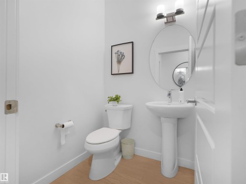 Modern bathroom featuring a white pedestal sink, circular vanity mirror, and brushed nickel light fixture - 22650 99A Avenue Nw, Edmonton, AB - Indoor Photo Showing Bathroom