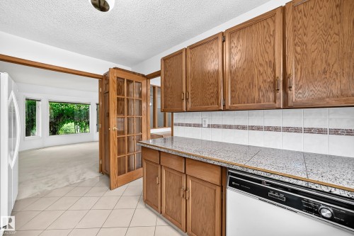 Kitchen featuring wood-finish cabinetry, speckled countertops, tile backsplash, and tile flooring - 17915 99A Avenue Nw, Edmonton, AB 