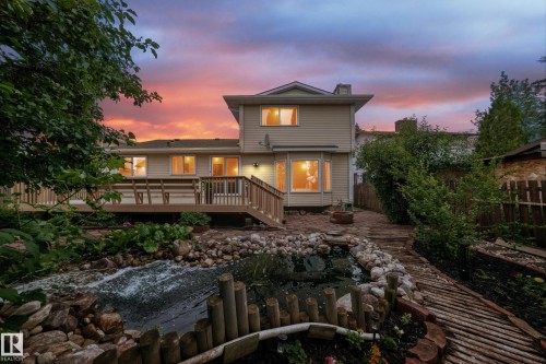Expansive rear deck with wood railing, leading to a stone-lined water feature and a pathway - 17915 99A Avenue Nw, Edmonton, AB 