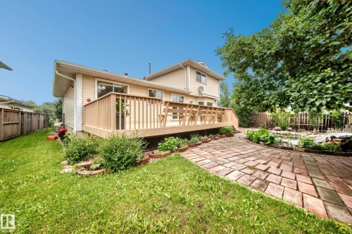 Spacious wood deck with railing, brick paver patio, lush green lawn, and mature trees - 17915 99A Avenue Nw, Edmonton, AB 