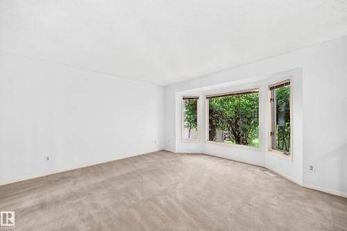 Expansive room featuring a bay window looking out to a well established and mature grape vine, neutral carpet, and white painted walls - 17915 99A Avenue Nw, Edmonton, AB 