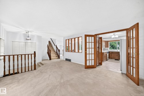 Neutral carpeted flooring, French doors leading to kitchen, wood-finish staircase, and built-in closet storage - 17915 99A Avenue Nw, Edmonton, AB 