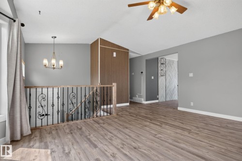 Open-concept living space with wood-finish flooring, a decorative staircase with wrought iron balusters, and a modern chandelier - 9530 174 Avenue Nw, Edmonton, AB - Indoor Photo Showing Other Room