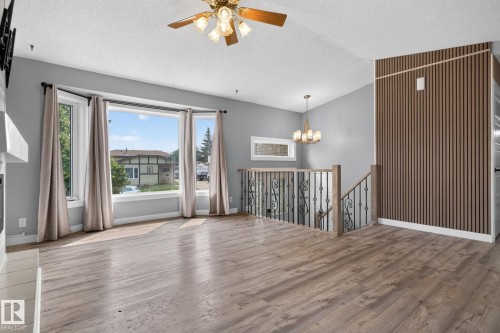 Spacious living area featuring wood-finish flooring, a decorative accent wall, a bay window, a ceiling fan with integrated lighting, and a staircase with an ornamental metal railing - 9530 174 Avenue Nw, Edmonton, AB - Indoor Photo Showing Other Room