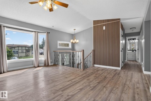 Spacious open-concept room featuring wood-finish flooring, large windows, a ceiling fan with integrated lighting, and a modern chandelier - 9530 174 Avenue Nw, Edmonton, AB - Indoor Photo Showing Other Room