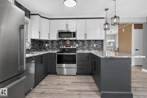 Contemporary kitchen featuring two-tone cabinetry, stainless steel appliances, a mosaic tile backsplash, light-toned wood-finish flooring, and pendant lighting - 9530 174 Avenue Nw, Edmonton, AB - Indoor Photo Showing Kitchen With Upgraded Kitchen
