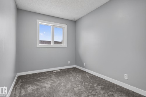 Spacious room featuring a large window, gray wall paint, textured ceiling, white trim, and gray carpet flooring - 9530 174 Avenue Nw, Edmonton, AB - Indoor Photo Showing Other Room