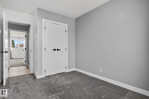 Neutral gray walls with white trim, gray patterned carpet, and white bi-fold doors with matte black hardware - 9530 174 Avenue Nw, Edmonton, AB - Indoor Photo Showing Other Room