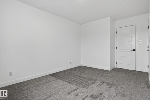Spacious room featuring gray textured carpeting, neutral white walls, and a five-panel interior door with matte black hardware - 9530 174 Avenue Nw, Edmonton, AB - Indoor Photo Showing Other Room
