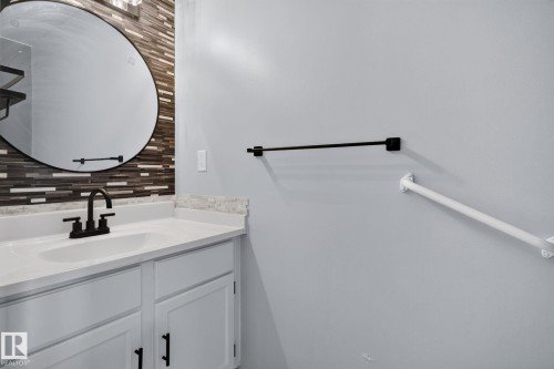 Bathroom vanity featuring a white countertop with an integrated sink, dark bronze faucet, and white shaker-style cabinetry - 9530 174 Avenue Nw, Edmonton, AB - Indoor Photo Showing Bathroom
