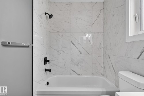 Bathtub with matte black fixtures, white marble-look tile surround, and a white framed window - 9530 174 Avenue Nw, Edmonton, AB - Indoor Photo Showing Bathroom