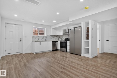 Open-concept kitchen area featuring wood-finish flooring, white cabinetry, and stainless steel appliances - 9530 174 Avenue Nw, Edmonton, AB - Indoor Photo Showing Kitchen