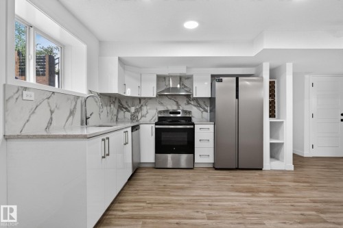 Modern kitchen featuring white cabinetry, stone countertops, a large window, stainless steel appliances, and wood-finish flooring - 9530 174 Avenue Nw, Edmonton, AB - Indoor Photo Showing Kitchen With Upgraded Kitchen