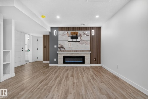 Contemporary living space featuring a built-in electric fireplace with a stone-look surround and a large-format tile accent wall - 9530 174 Avenue Nw, Edmonton, AB - Indoor Photo Showing Living Room With Fireplace