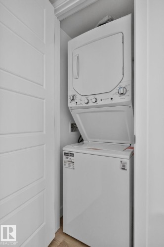 Dedicated laundry closet featuring a white stacked washer and dryer unit, white paneled bifold doors, and light wood-finish flooring - 9530 174 Avenue Nw, Edmonton, AB - Indoor Photo Showing Laundry Room