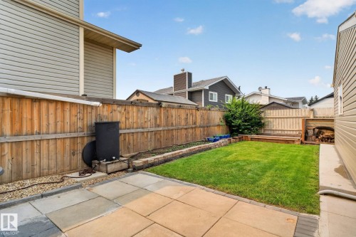 Landscaped backyard featuring a paver patio, a green lawn, a wooden privacy fence, and a wood storage area - 9530 174 Avenue Nw, Edmonton, AB - Outdoor With Exterior