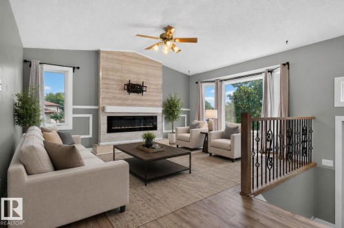Living area featuring a vaulted ceiling with a fan, a stone-clad fireplace with an electric insert, a bay window, and a wood-finish floor extending to a decorative wrought iron and wood railing - 9530 174 Avenue Nw, Edmonton, AB - Indoor Photo Showing Living Room With Fireplace