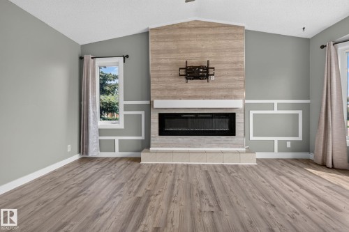 Living area featuring a modern electric fireplace with a wood-finish accent wall, tile hearth, and white mantel - 9530 174 Avenue Nw, Edmonton, AB - Indoor Photo Showing Living Room With Fireplace
