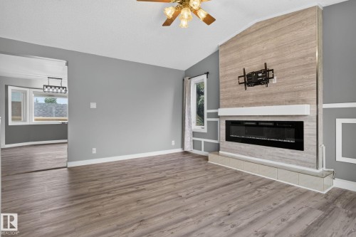 Spacious living area featuring wood-finish flooring, a contemporary electric fireplace with a white mantel, and an accent wall with a wood-look finish - 9530 174 Avenue Nw, Edmonton, AB - Indoor Photo Showing Living Room With Fireplace