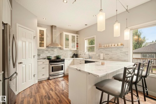 Kitchen featuring a stainless steel range, white cabinetry, a large kitchen island with seating, a tile backsplash, and wood-finish flooring - 1660 Tomlinson Common Nw, Edmonton, AB 