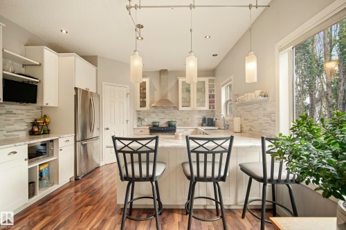 Wood-finish flooring, white cabinetry, stainless steel appliances, marble-finish countertops, and a full tile backsplash - 1660 Tomlinson Common Nw, Edmonton, AB 