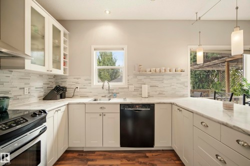 Well-appointed kitchen featuring white cabinetry, stone countertops, a tile backsplash, wood-finish flooring, and pendant lighting - 1660 Tomlinson Common Nw, Edmonton, AB 