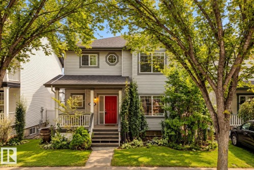 Light gray siding exterior with a red entry door, covered porch, multiple windows, and front landscaping - 1660 Tomlinson Common Nw, Edmonton, AB 