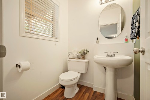 Pedestal sink with chrome fixtures, oval mirror, window with blinds, and wood-finish flooring - 1660 Tomlinson Common Nw, Edmonton, AB 