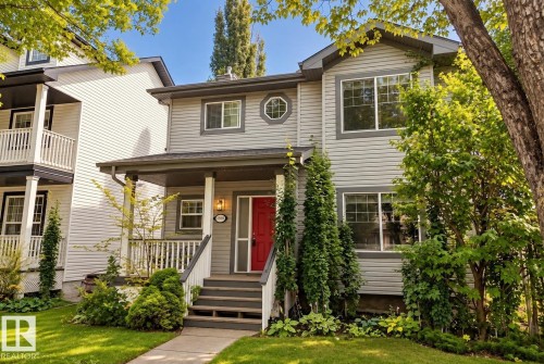 Two-story exterior with light gray siding, dark trim, and a covered front porch featuring a red entry door - 1660 Tomlinson Common Nw, Edmonton, AB 