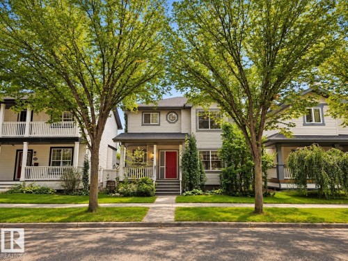 Two-story residence featuring light-toned siding, a covered front porch, and a contrasting red entry door - 1660 Tomlinson Common Nw, Edmonton, AB 