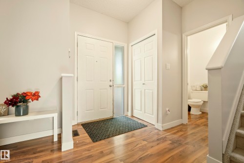 Entryway featuring wood-finish flooring, a solid panel entry door with a frosted sidelight, and a double-door closet - 1660 Tomlinson Common Nw, Edmonton, AB 
