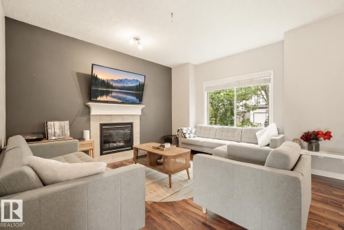 Living area featuring wood-finish flooring, a fireplace with a mantel, and a large window - 1660 Tomlinson Common Nw, Edmonton, AB 