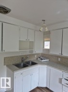 White cabinetry with upper and lower storage, dual basin stainless steel sink, tiled backsplash, and wood-finish flooring - 