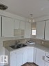 White cabinetry with upper and lower storage, dual basin stainless steel sink, tiled backsplash, and wood-finish flooring - 12005 45 Street Nw, Edmonton, AB 
