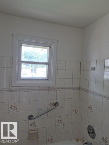 Window with white trim, tiled wall surround with decorative accents, and a built-in grab bar - 12005 45 Street Nw, Edmonton, AB 