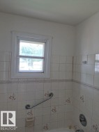 Window with white trim, tiled wall surround with decorative accents, and a built-in grab bar - 
