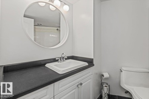 White vanity with ample cabinet storage, dark countertop, and integrated sink with chrome faucet - #702 10045 117 St Nw, Edmonton, AB 