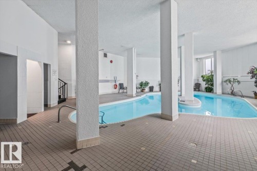 Indoor swimming pool with light blue water, surrounded by gray tile flooring, and white support columns - #702 10045 117 St Nw, Edmonton, AB 