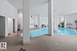 Indoor swimming pool with light blue water, surrounded by gray tile flooring, and white support columns - 