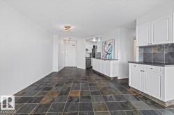 Stone tile flooring, white shaker-style cabinetry, dark countertops, and a tile backsplash - 