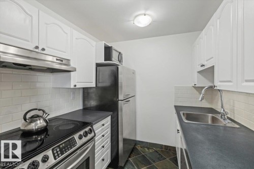 Kitchen featuring white cabinetry, subway tile backsplash, dark countertops, built-in stainless steel appliances, and slate tile flooring - #702 10045 117 St Nw, Edmonton, AB 