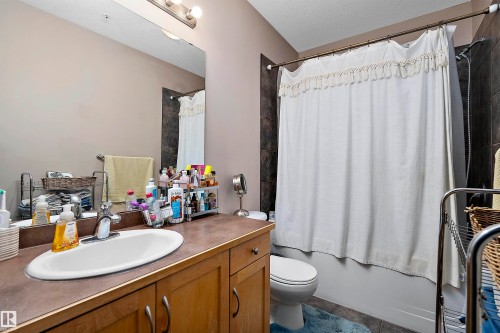 Bathroom featuring a wood-finish vanity with an integrated sink, a large wall-mounted mirror, and a tub-shower combination with dark tile surround - #713 10503 98 Av Nw, Edmonton, AB - Indoor Photo Showing Bathroom