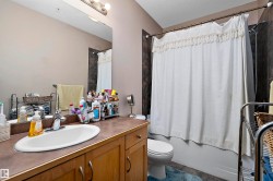 Bathroom featuring a wood-finish vanity with an integrated sink, a large wall-mounted mirror, and a tub-shower combination with dark tile surround - 