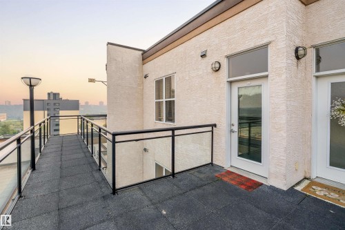 Spacious exterior balcony featuring textured stucco siding, glass panel railings with black frames, and durable dark-toned tile flooring - #713 10503 98 Av Nw, Edmonton, AB - Outdoor With Balcony With Exterior