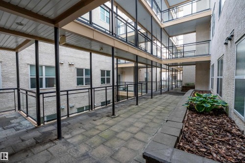 Courtyard with paver stone pathways, multiple levels of balconies with glass railings, and ground-level planter boxes - #713 10503 98 Av Nw, Edmonton, AB - Outdoor With Balcony With Exterior