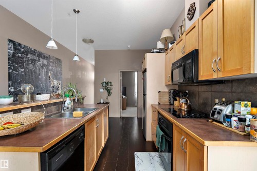 Contemporary kitchen with dark wood-finish flooring, light wood cabinetry, and contrasting dark countertops - #713 10503 98 Av Nw, Edmonton, AB - Indoor Photo Showing Kitchen With Double Sink