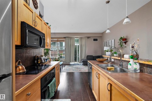 Open-concept kitchen featuring wood-finish cabinetry, built-in microwave, dark tile backsplash, and a double basin sink - #713 10503 98 Av Nw, Edmonton, AB - Indoor Photo Showing Kitchen With Double Sink