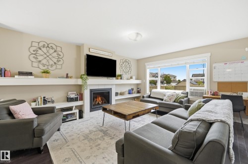 Living area featuring a fireplace with a white tile surround, built-in shelving, wood-finish flooring, and a large picture window - 1564 36 Avenue Nw, Edmonton, AB 