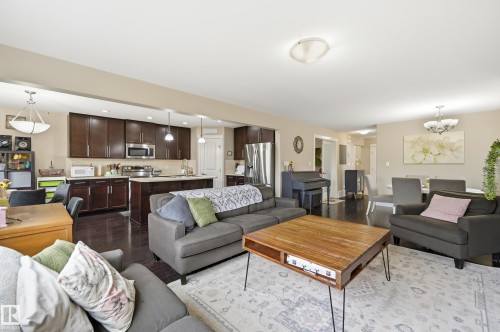 Open-concept living area with dark wood-finish flooring, recessed lighting, and a kitchen featuring dark cabinetry, stainless steel appliances, and an island - 1564 36 Avenue Nw, Edmonton, AB 